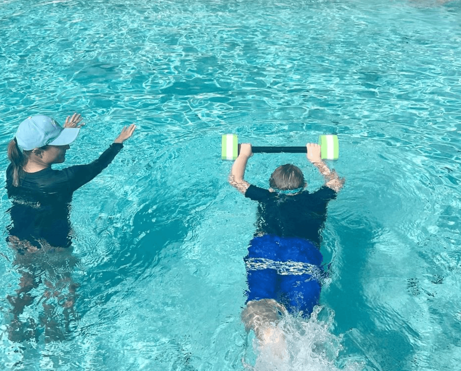 Dr. Amanda Clarke teaching a boy to kick with a barbell float across a sunlit pool